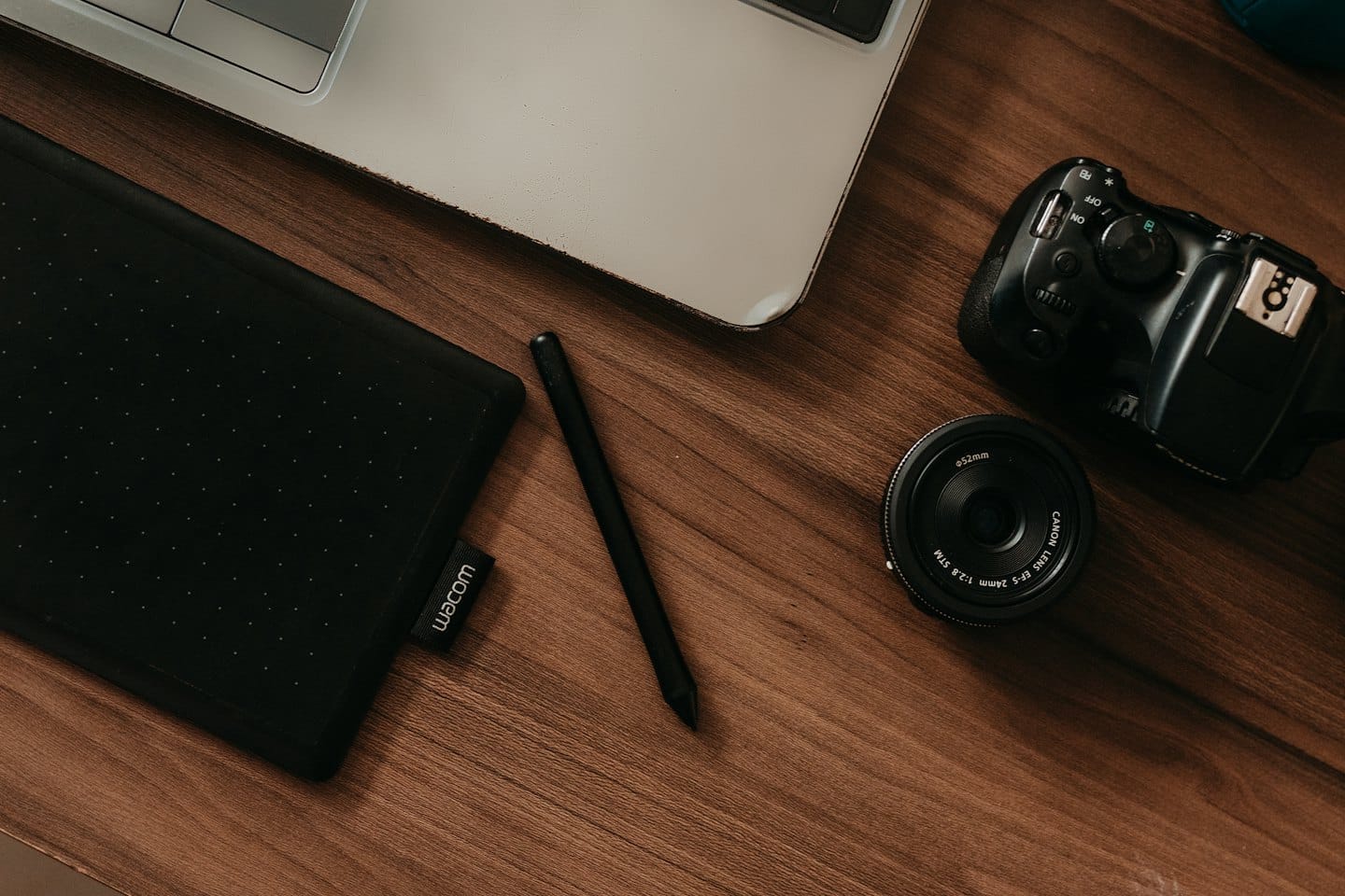 Na drevenom stole je notebook, grafický tablet, stylus a fotografické vybavenie.