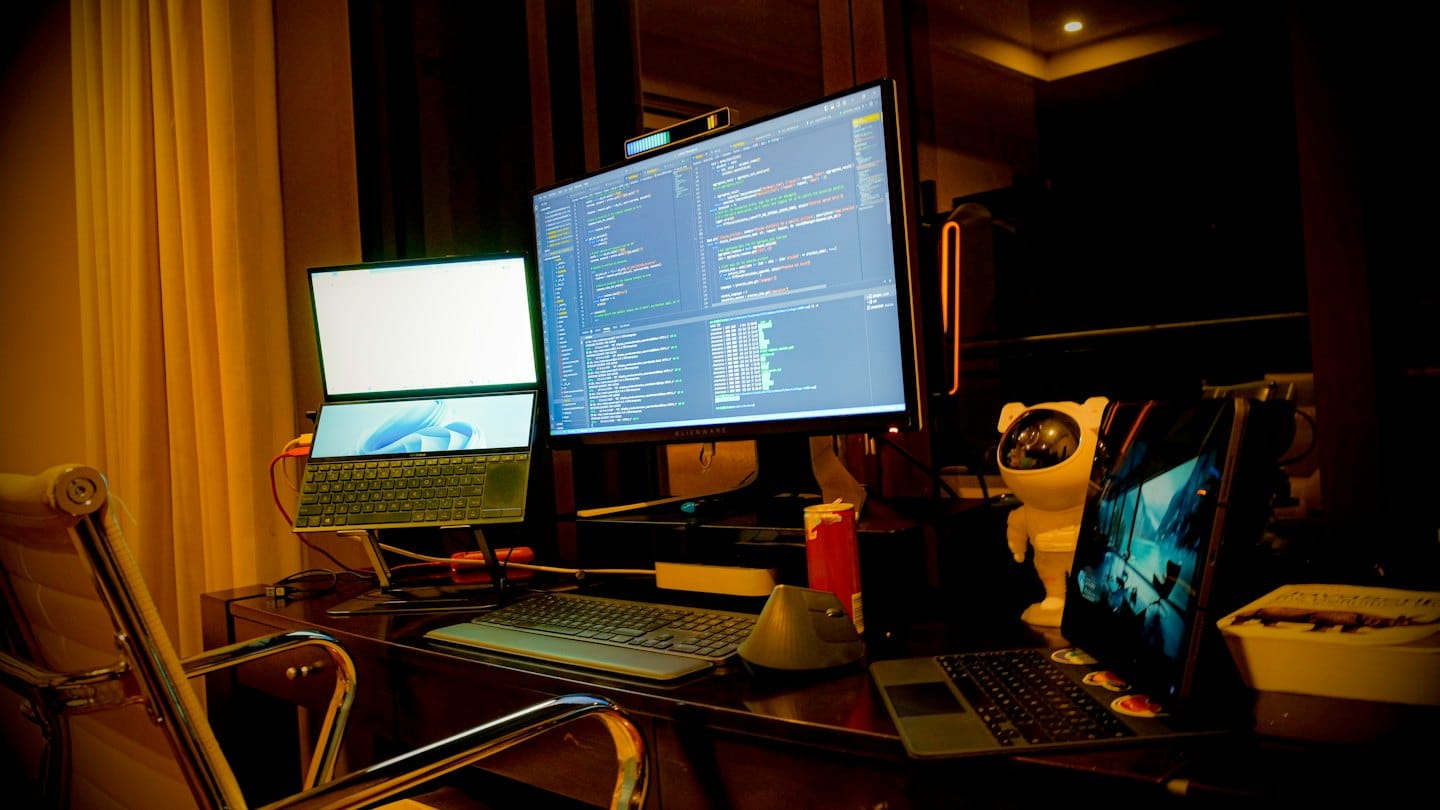 Na tmavom drevenom stole sú zobrazené monitory s programovacím kódom.